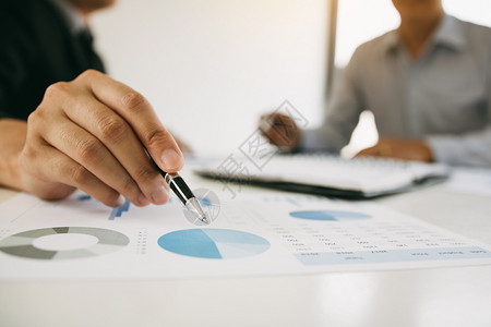 财务图一名商人拿着笔指向财务报表或公司利润图并在办公室桌上分析背景