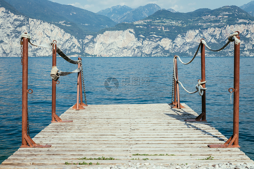 Wooden码头横跨蓝湖水在LagodiGarda山上图片