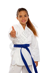 空手道制服穿着白色和服的空手道女孩和蓝腰带显示一个完全举起拇指的标志背景