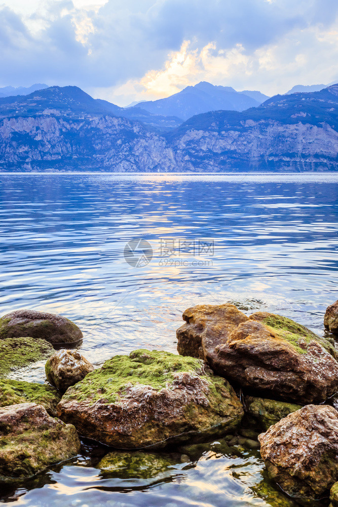 在LagodiGarda湖中有各种岩石和反射物清澈的水山和天空图片