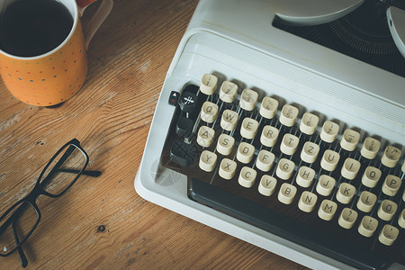 旧式打字机眼镜和木制桌上咖啡杯背景图片