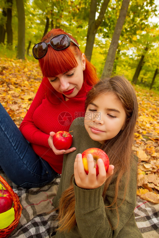 身穿明亮毛衣的年轻母亲和女儿在大自然野餐上吃苹果图片