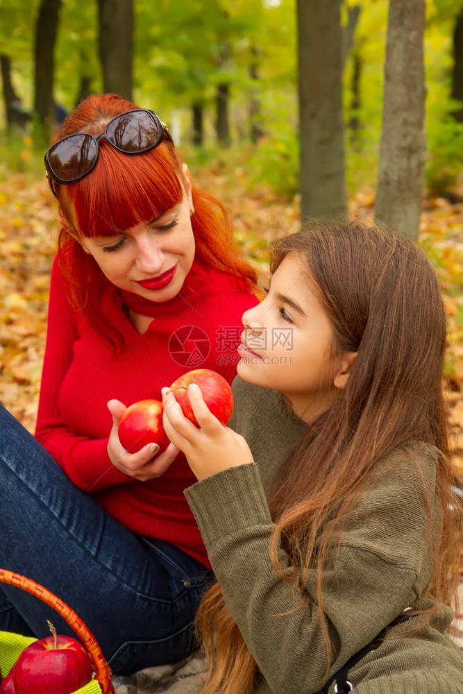 身穿明亮毛衣的年轻母亲和女儿在大自然野餐上吃苹果图片