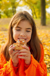 穿着明亮橙色毛衣的小女孩在自然野餐上吃美味的自制蛋糕图片