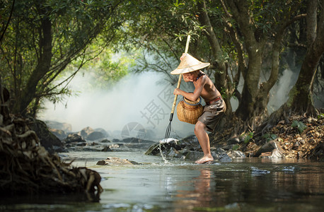 江河上的年轻男孩渔民鱼叉中的背景图片