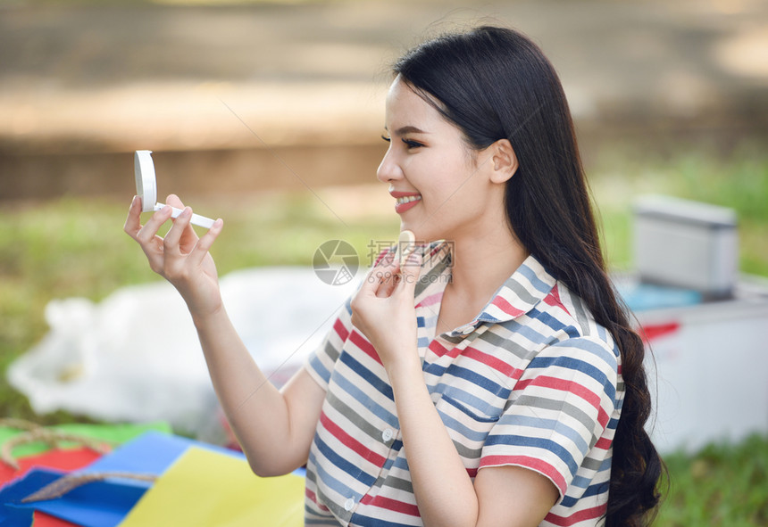 镜中女人化妆品美丽笑的年轻女孩亲自在露天公园外地做面粉图片