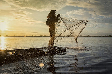 亚洲渔民利用木船净网捕捞在河中投下净日落或Silhouette渔民站在农村的船人上背景图片
