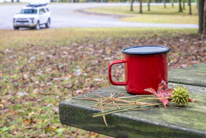 野餐桌上的金属茶杯、背景有一辆SUV车的森林停场、旅行和驾驶概念图片