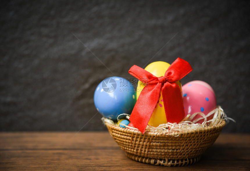 复活节鸡蛋在生锈桌木和黑暗背景的巢篮中有红丝弓图片