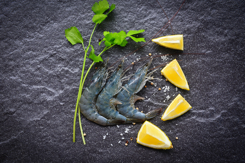 黑盘上生虾在海产食品餐馆用暗底背景的香料柠檬烹饪新鲜虾图片