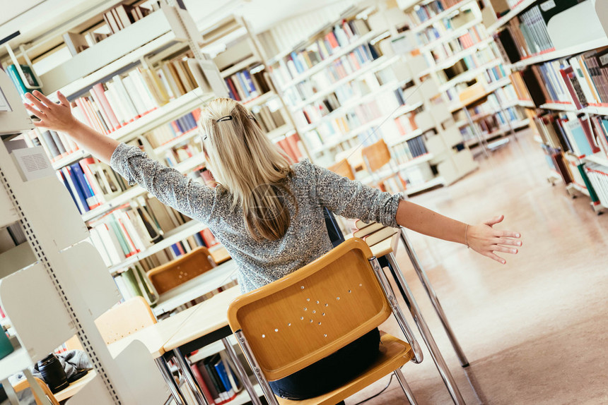 厌倦的女学生坐在书桌前有一堆还大学图馆图片