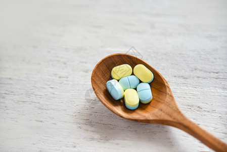 药片店白木桌面底的木勺中黄色和蓝的药片抗生素背景图片