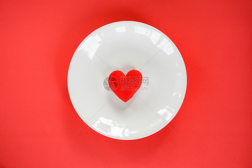 红心放在白色盘子的浪漫桌上装饰在红色纹理背景的顶层视野上图片