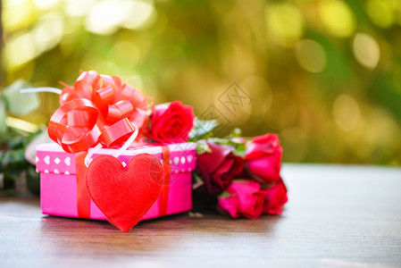 情人节礼物盒花爱概念粉红礼物盒带丝弓红玫瑰花和心放在木桌上绿色背景图片