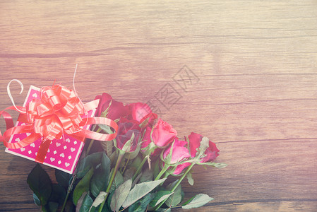 粉红礼物盒带丝弓红玫瑰花在木制桌子上生锈的背景语调图片