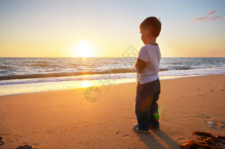 海滩上的孩子看着海日落概念场景图片