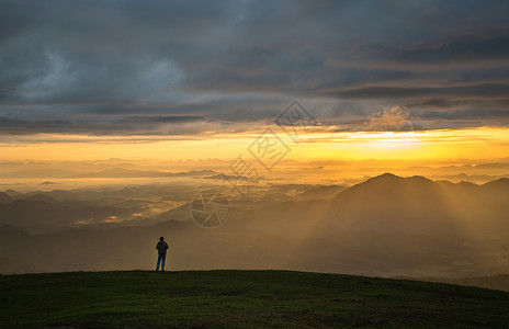 山顶上成功的男子徒山上站着日出地貌山上的人有雾黄天空山上月光照亮背景图片