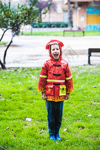 男孩打扮成消防员雨衣在天公园的草地上喷洒图片