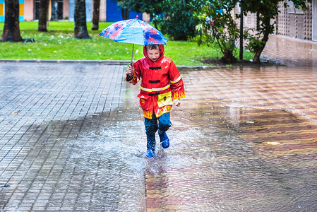 穿着红色雨衣的男孩伪装成雨伞喷洒在水坑里高清图片