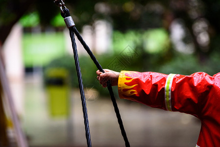 儿童带着红雨衣消防员紧抓住绳子在雨中游乐场图片