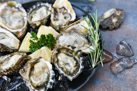 黑板背景的新鲜牡蛎海露天牡蛎贝壳配有草药香料柠檬迷迭面糖在餐厅美食中桌和冰上健康的海鲜生牡蛎食品背景图片