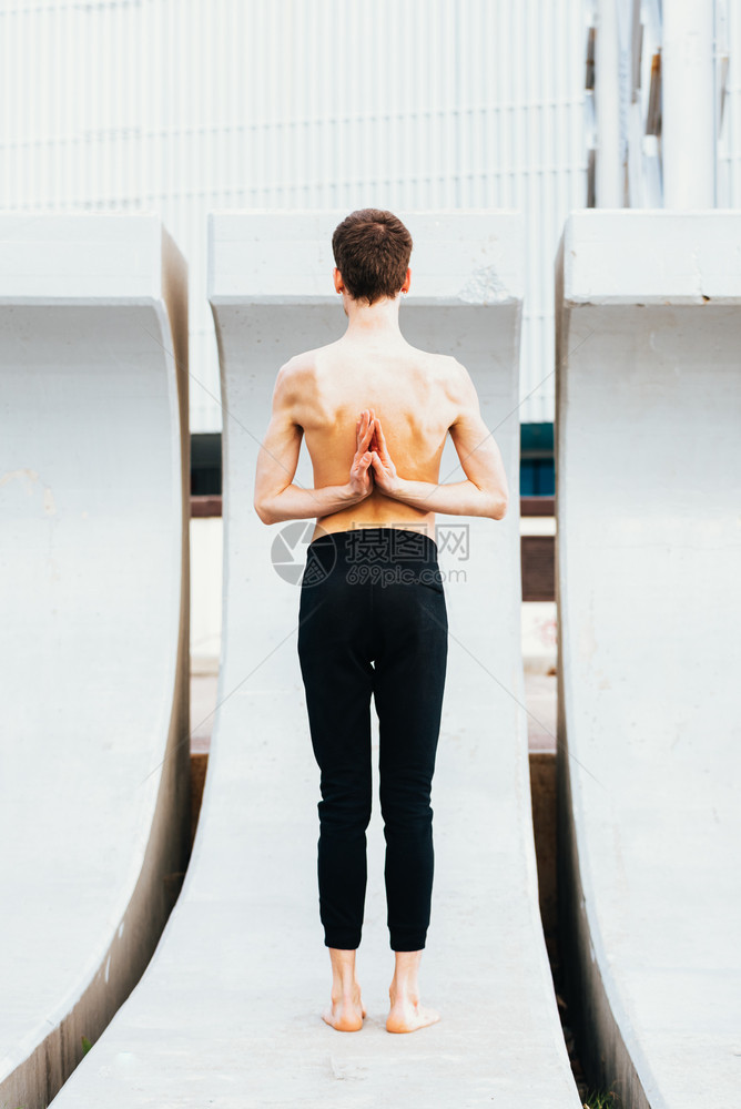 瑜伽的姿势倒着祈祷或用Namaste手背对着一个年轻人在户外表演的背部图片