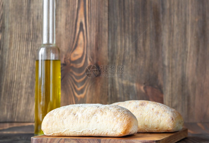 Ciabatatta意大利白面包木底有一瓶橄榄油图片