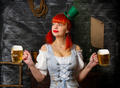 啤酒狂欢节穿着小妖精帽子的年轻红头发爱尔兰女服务员在圣帕特里克日酒吧带了两杯泡沫啤酒背景