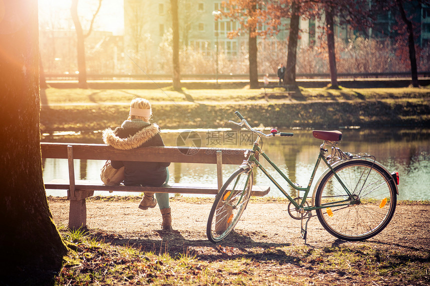 春时在公园长椅上享受阳光的骑自行车年轻女子背影图片
