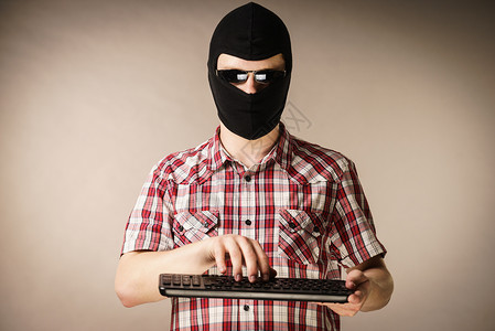 疯狂的黑客男人穿着色的balaclava拿着电脑键盘网上的仇恨言论背景图片