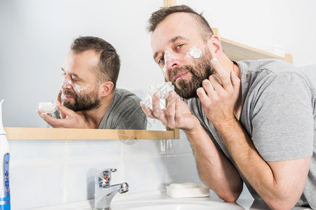 男人在浴室镜子前脸上涂满了香水男人在浴室里涂了润湿霜图片