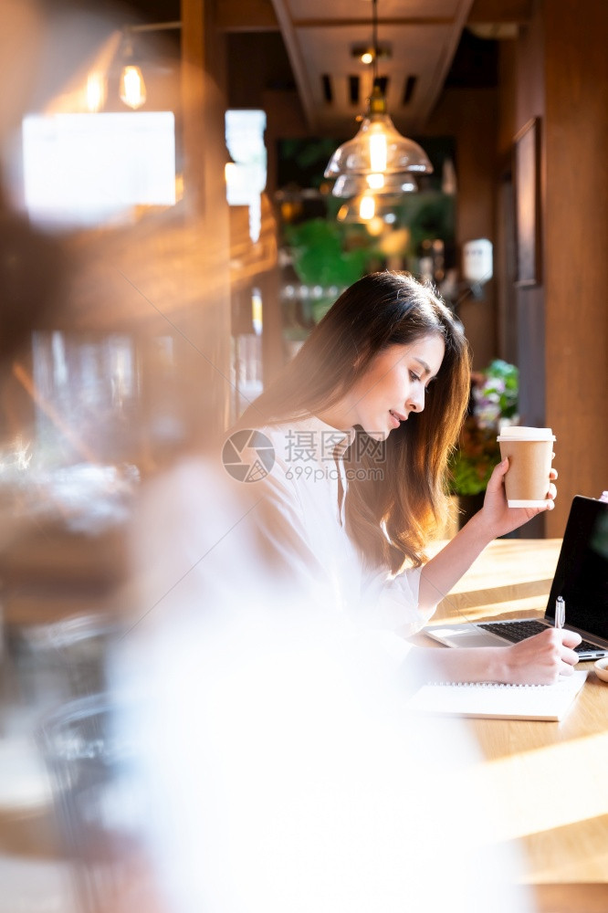 身着智能散装服的年轻亚洲女在客厅工作使用笔记本电脑在家工作喝热咖啡和羊角面包图片
