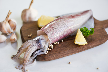 切菜板上的生鱿鱼和白板背景的沙拉香料加柠檬大蒜新鲜乌贼章鱼或餐饮海鲜市场煮熟食品的鱼背景图片