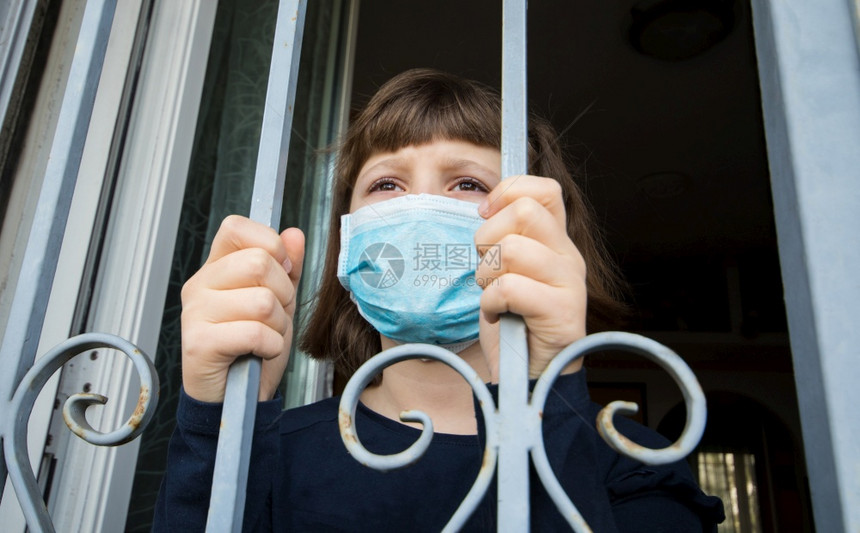 家中隔离的年轻女孩自动隔离身戴面罩保护从窗户向外看的疾传播图片
