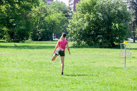 玩射击在公园里玩飞盘高尔夫运动游戏的年轻女子背景