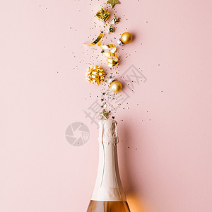 彩带星圣诞球和彩蛋的金装饰品从香槟酒瓶中飞来平躺节日概念欢庆香槟酒瓶和粉红背景的金装饰品背景图片