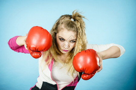 穿着红色拳击手套试图打斗工作室拍摄蓝背景穿着拳击手套的有趣女人图片