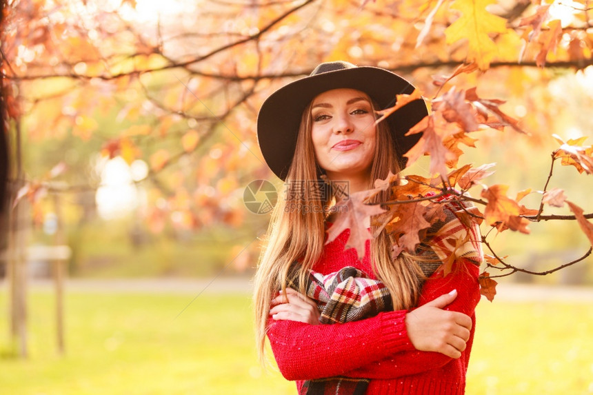 公园的秋季颜色概念女人站在树边穿着黑帽子和红色天候的迷人女士和非常时髦的围巾女人站在树边图片
