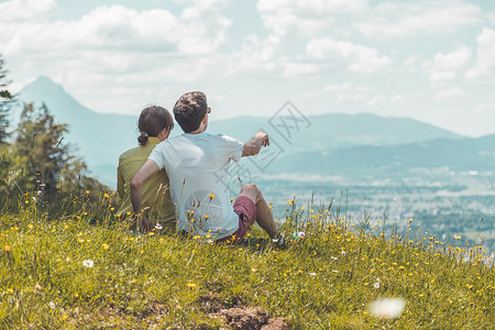 高山症来远足旅行的夫妇坐在草地上享受远城风景背景