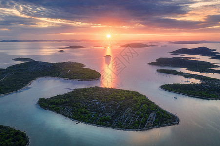 克罗地亚夏季日落时得里海美丽的小岛空中景象蓝水山上的绿树多彩天空云和橙色的太阳背景图片