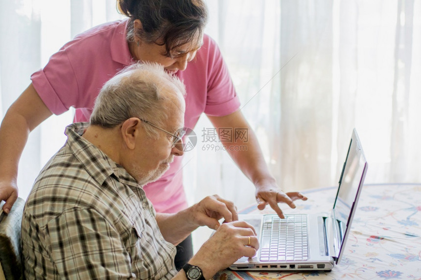 年长男子和他的看护者在家里花时间用笔记本电脑陪着Gegeter图片