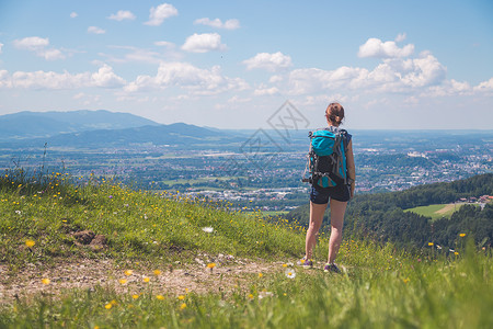 高山症徒步旅行的体育女运动员站在草地上享受远城风景背景