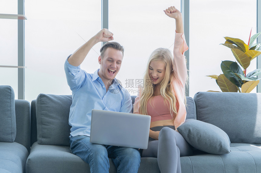 微笑的生意金发白夫妇放松使用电脑笔记本在家里工作和沙发上聊天花时间在隔离冠状概念图片