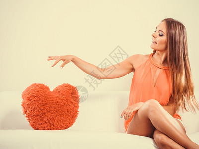 坐在白沙发上穿着红色心型枕头的漂亮年轻女孩情人节的爱图片