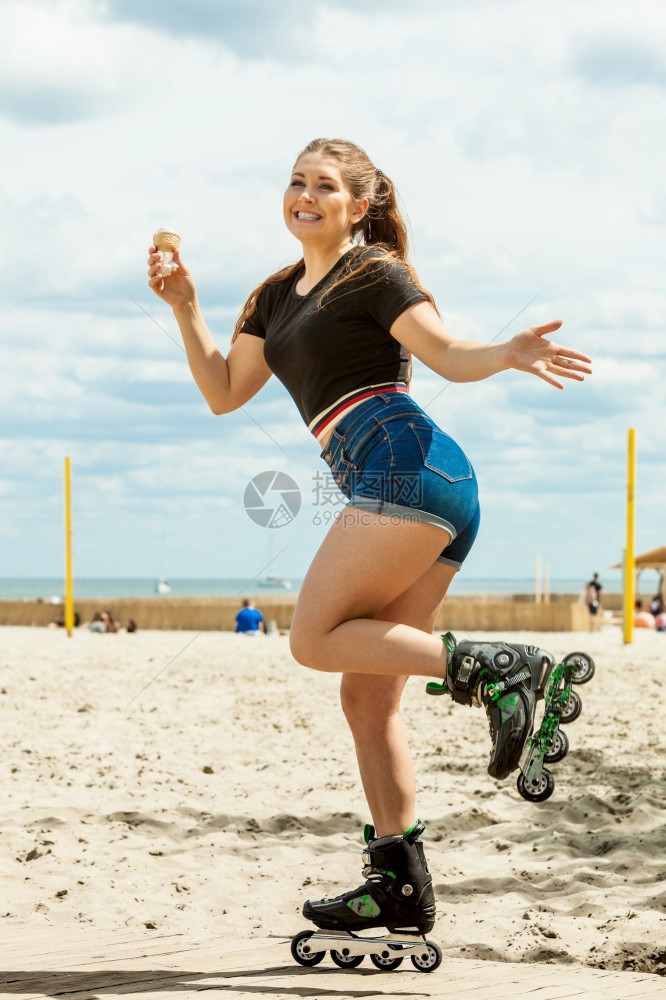 快乐的女子穿着溜冰鞋享受她的空闲时间同在夏日阳光明媚的海滩天气中吃冰淇淋图片