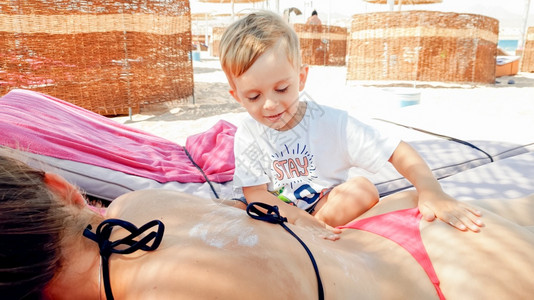 照片三岁小男孩在海边的太阳床上给年轻母亲按摩图片
