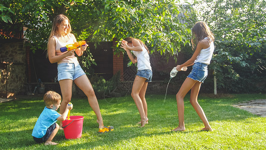 欢笑的家庭在后院用水和花园龙头泼的照片人们在炎热的阳光夏日玩耍和乐图片