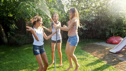 家庭在夏季户外玩耍和乐穿着湿衣服的女孩在花园水管下跳舞和家庭在户外玩耍和乐家庭在花园水管下跳舞和夏天高清图片素材