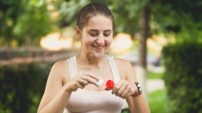 日落时在公园吹肥皂泡沫的美丽微笑年轻女子肖像图片