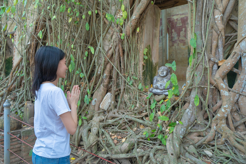 在泰国SamutSongkhram区的WatBangKung透过窗户用旧砖墙和树根向金佛像祈祷或许愿图片